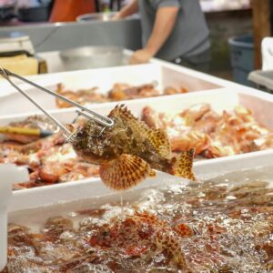 A sculpin fish being picked with tongs at an indoor market.