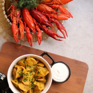 Appetizing seafood platter featuring bright red crayfish, dumplings, and sour cream dip served on a wooden board.