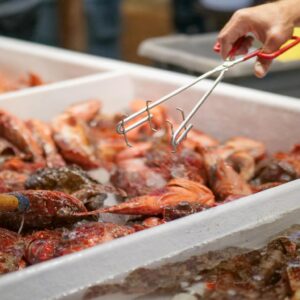 Fresh sculpin on ice at a seafood market with a hand using tongs to select fish.