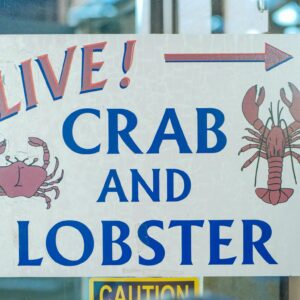 Sign advertising live crab and lobster with colorful illustrations at a seafood market.